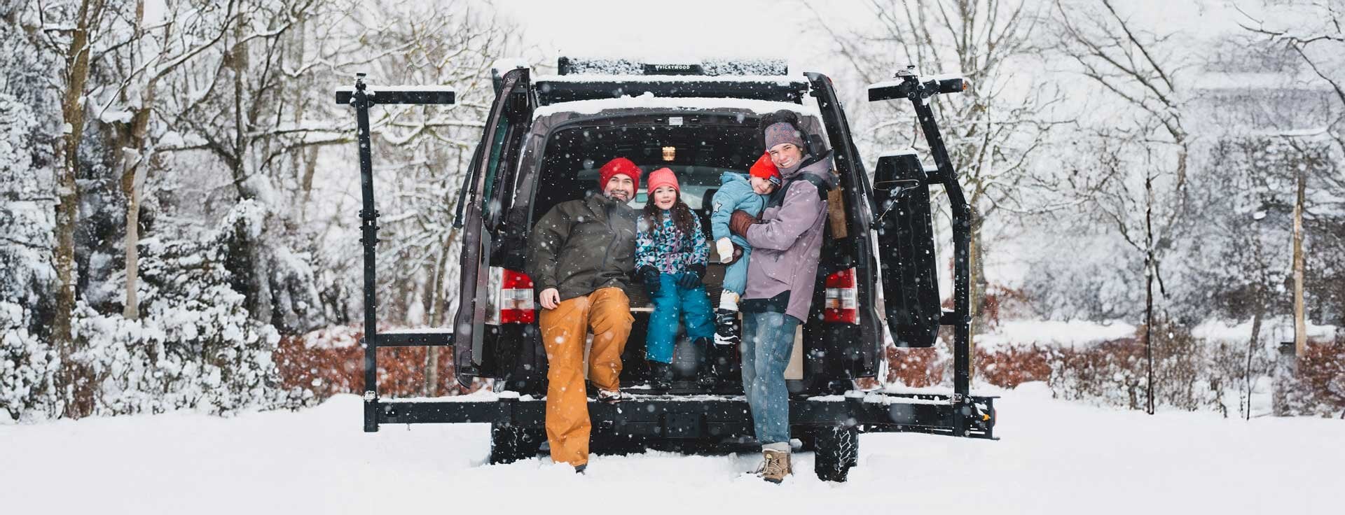 Vierköpfige Familie mit Campervan und Dachzelt im Winterurlaub.