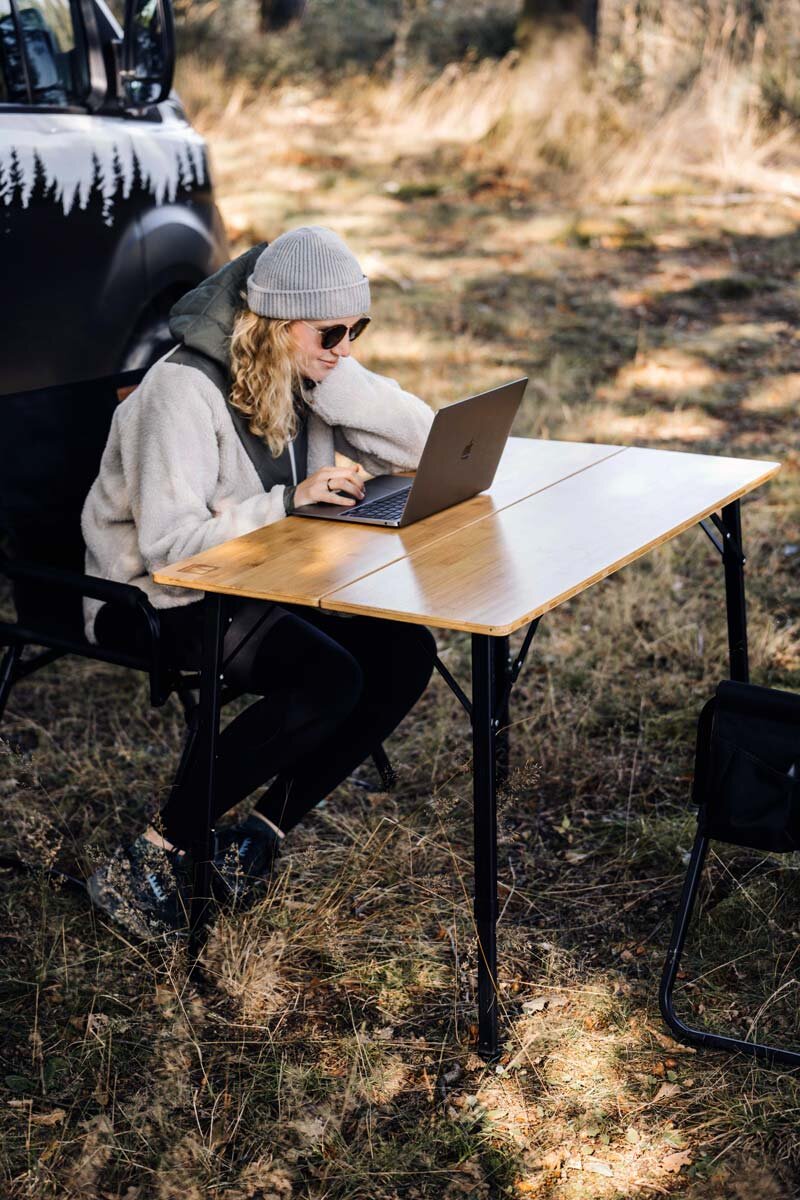 Mädchen sitzt mit ihrem Laptop an einem Campingtisch.